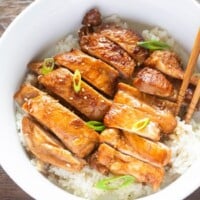 Sliced teriyaki chicken on rice with chopsticks on the side.