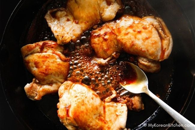 Spooning teriyaki sauce over chicken in a skillet.