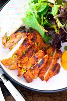 spicy gochujang chicken served on a white plate with green salad